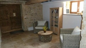 Una habitación rústica con paredes de piedra, una puerta de madera, muebles de mimbre y suelo de baldosas.