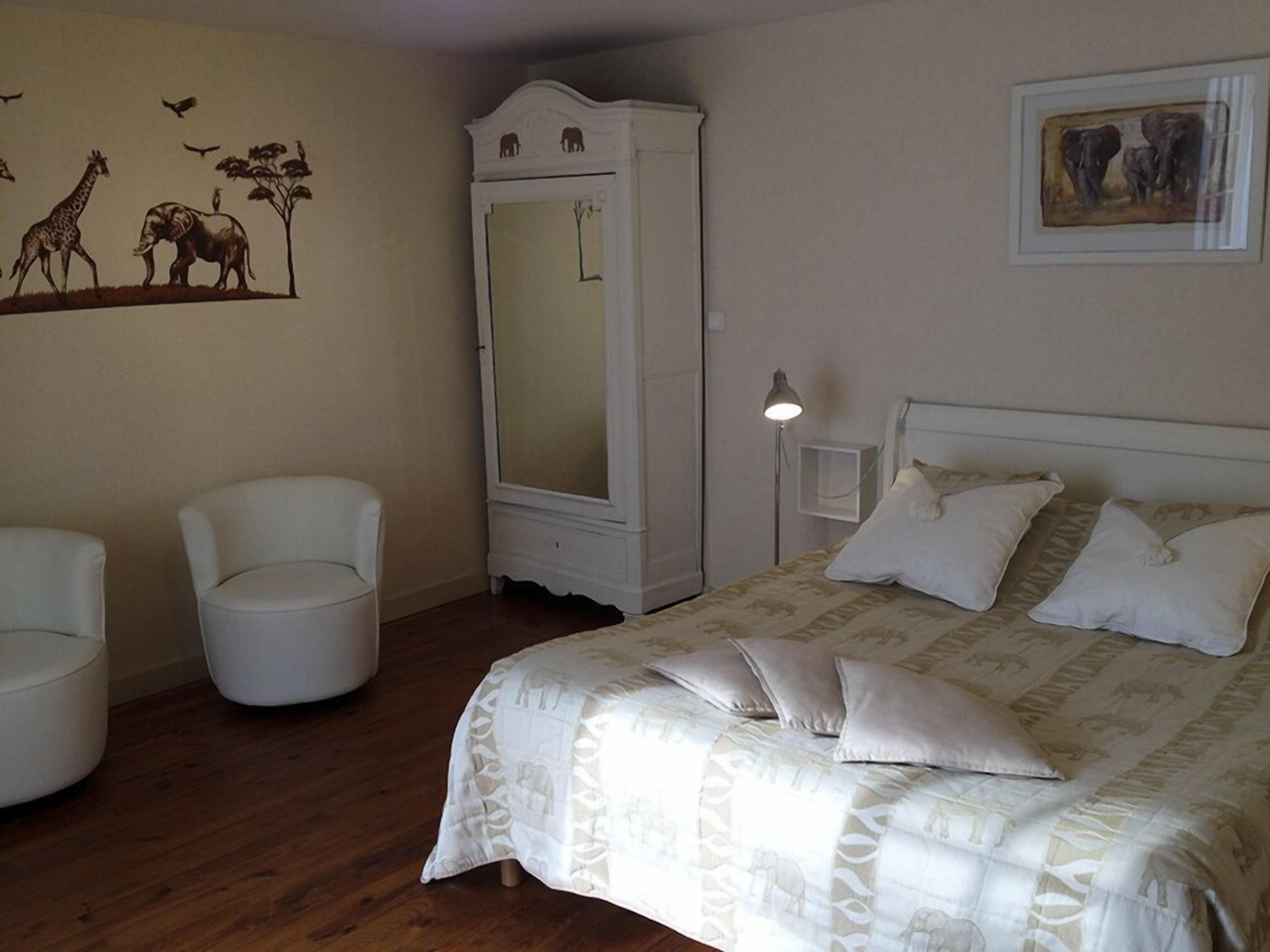 Un dormitorio con cama, dos sillas, armario y decoración en la pared.