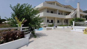 A multi-story building with a white facade, a balcony, and a pool area. - Maggana Residence (Kefalonia)