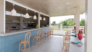 A long dining table with chairs, a bar area with hanging lights, and a view of greenery outside. - Maggana Residence (Kefalonia)