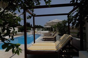 A poolside area with lounge chairs and a pergola. - Maggana Residence (Kefalonia)