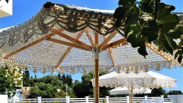 A pool area with lounge chairs and umbrellas, surrounded by a white fence and greenery. - Maggana Residence (Kefalonia)