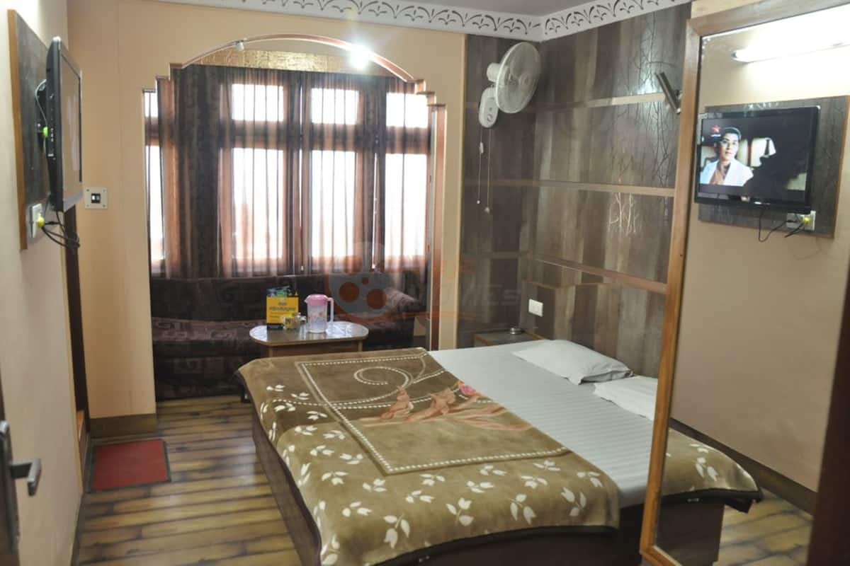 Habitación de hotel con cama, televisor, ventilador y ventana con cortinas.
