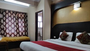 Quarto de hotel com uma cama grande, um sofá menor, cortinas estampadas e porta do banheiro visível.