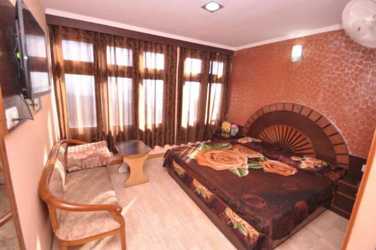 Un dormitorio con una cama, una silla de madera, una mesita y un televisor montado en la pared.
