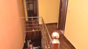 Corredor de hotel com escadaria de mármore, corrimão de metal e uma porta no final.