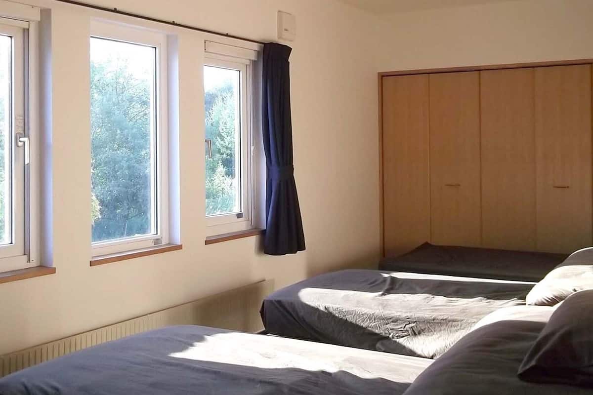 Un dormitorio con dos camas, un armario y tres ventanas.