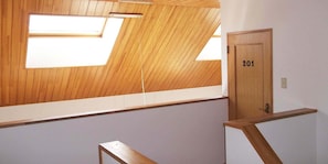 A room with a sloped ceiling, skylights, a wooden door labeled "201", and a small wooden bench. - Pension Yu Hokkaido (Ebetsu)