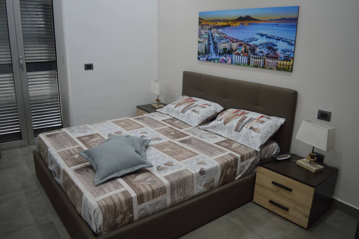A bedroom with a large bed, a nightstand, a lamp, and a painting on the wall.