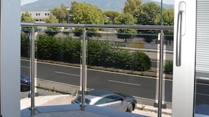 Une vue depuis un balcon doté d’une balustrade en métal, donnant sur une rue animée et sur une montagne en arrière-plan.