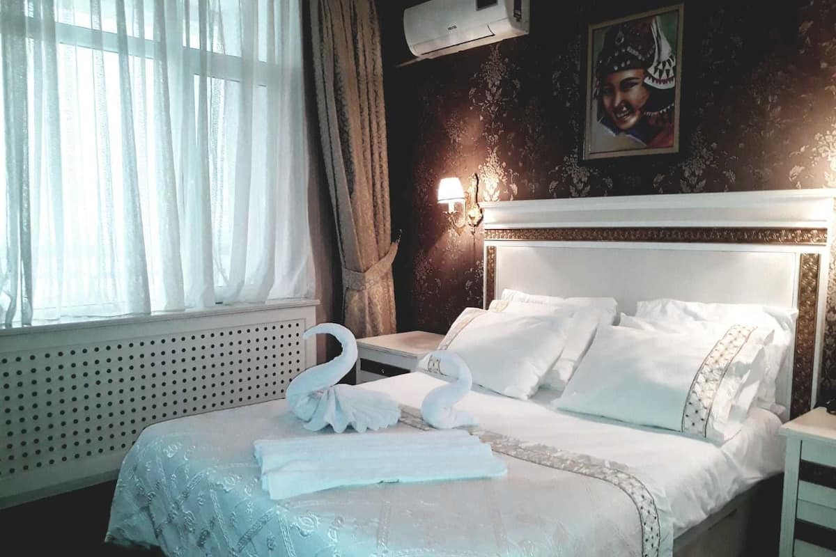 Quarto de hotel com uma cama bem arrumada, ar condicionado fixado na parede e luminária decorativa.