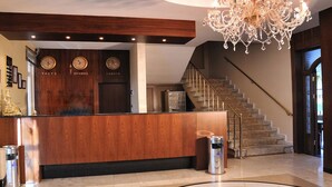 A reception area with a wooden counter, clocks displaying Tokyo, Istanbul, and London times, a chandelier, and a staircase. - Pelikan Otel (Istanbul)