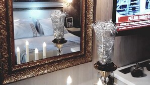 A hotel room with a large ornate mirror, a television, and a bedside table with candles and a decorative vase. - Pelikan Otel (Istanbul)