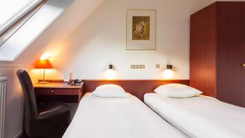 Een hotelkamer met twee enkele bedden, een bureau met stoel, een lamp en een ingelijste foto aan de muur.