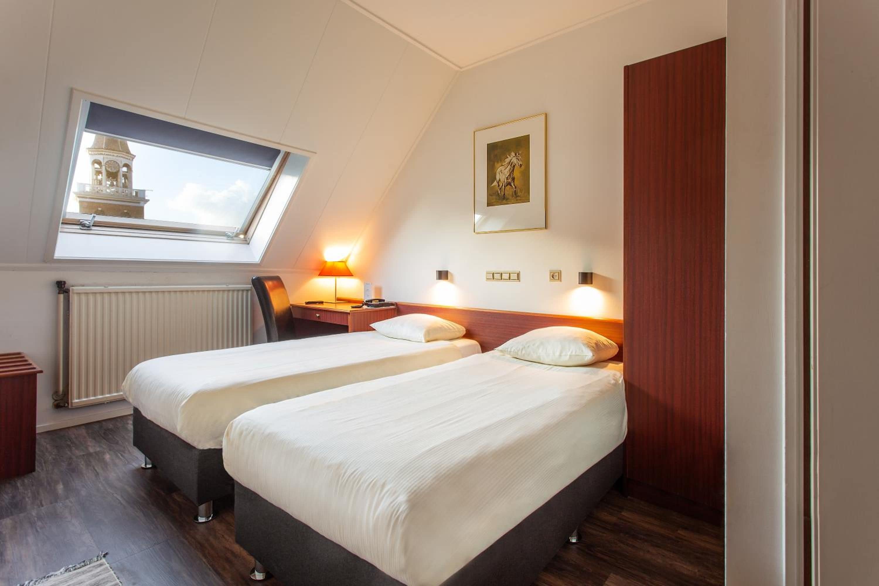 A hotel room with two beds, a skylight, a radiator, and a painting on the wall.