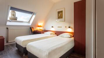 A hotel room with two beds, a skylight, a radiator, and a painting on the wall.