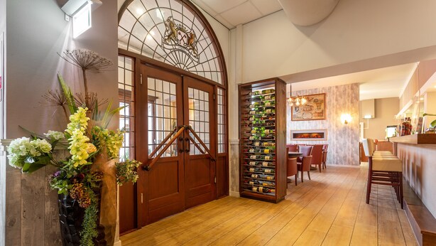 Un couloir au plancher de bois, avec une grande porte en bois, un porte-bouteilles fixé au mur et un coin salon comprenant des chaises et une table.