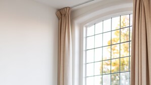 Une chambre moderne avec une grande fenêtre, un lit doté d’une tête de lit blanche et une table de chevet.
