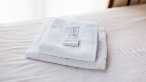 Une serviette blanche, soigneusement pliée, et une bouteille de lotion posées sur un lit.