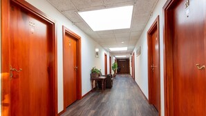 Un couloir d’hôtel avec des portes en bois numérotées 22 et 21, une table avec des chaises et des plantes en pot.