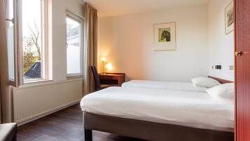 Ein Hotelzimmer mit einem großen Bett, einem Schreibtisch mit Lampe und einem Fenster mit Vorhängen.