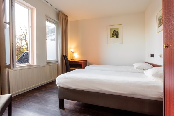 A hotel room with a large bed, a desk with a lamp, and a window with curtains. - Hotel Het Wapen Van Leiden (Appingedam)