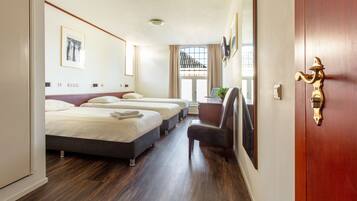 Habitación de hotel con tres camas, piso de madera, puerta con manija de bronce y ventana con vista a un balcón.