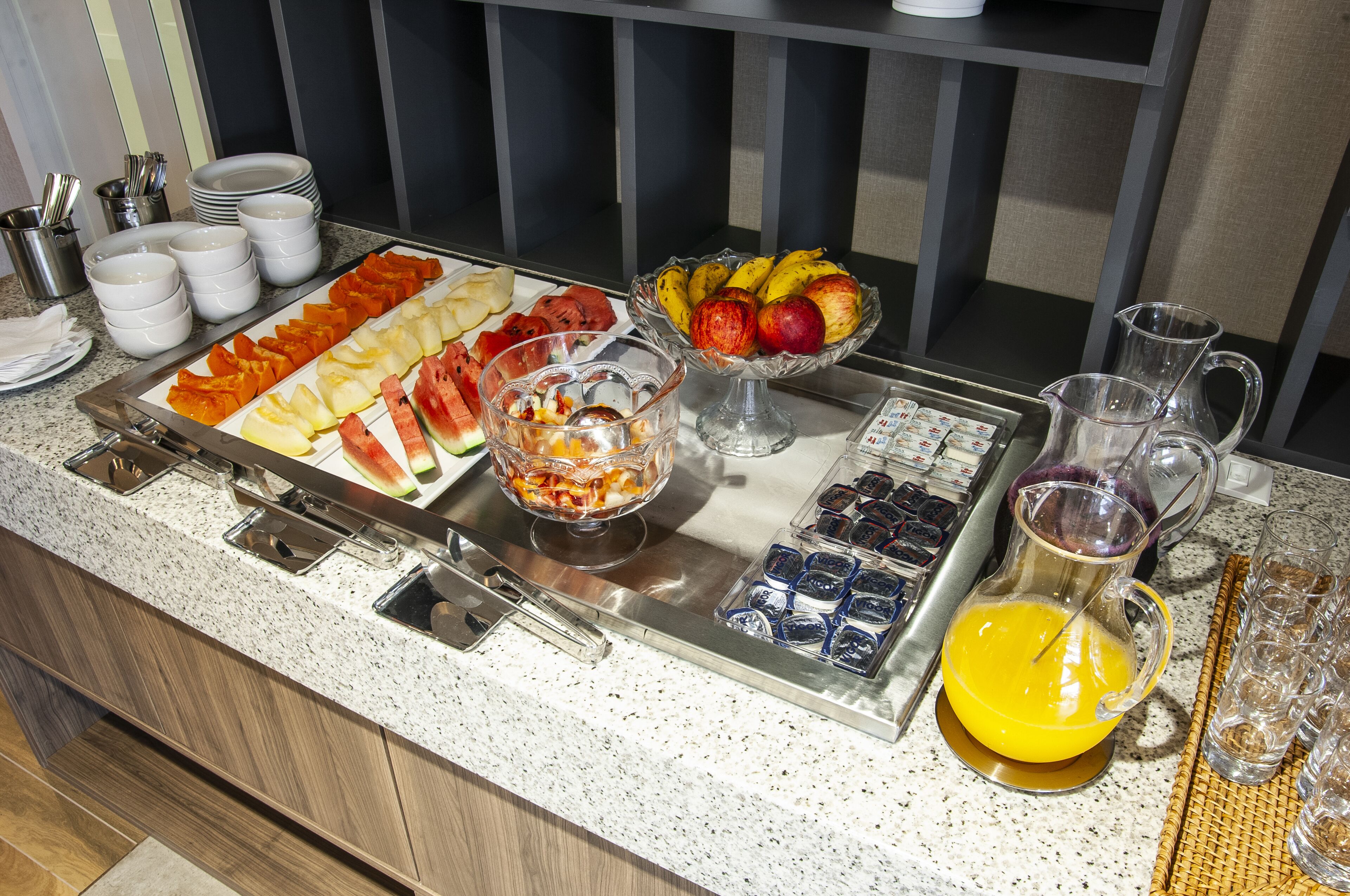 Un buffet proposant une variété de fruits, une carafe de jus d’orange et un plateau de divers aliments.