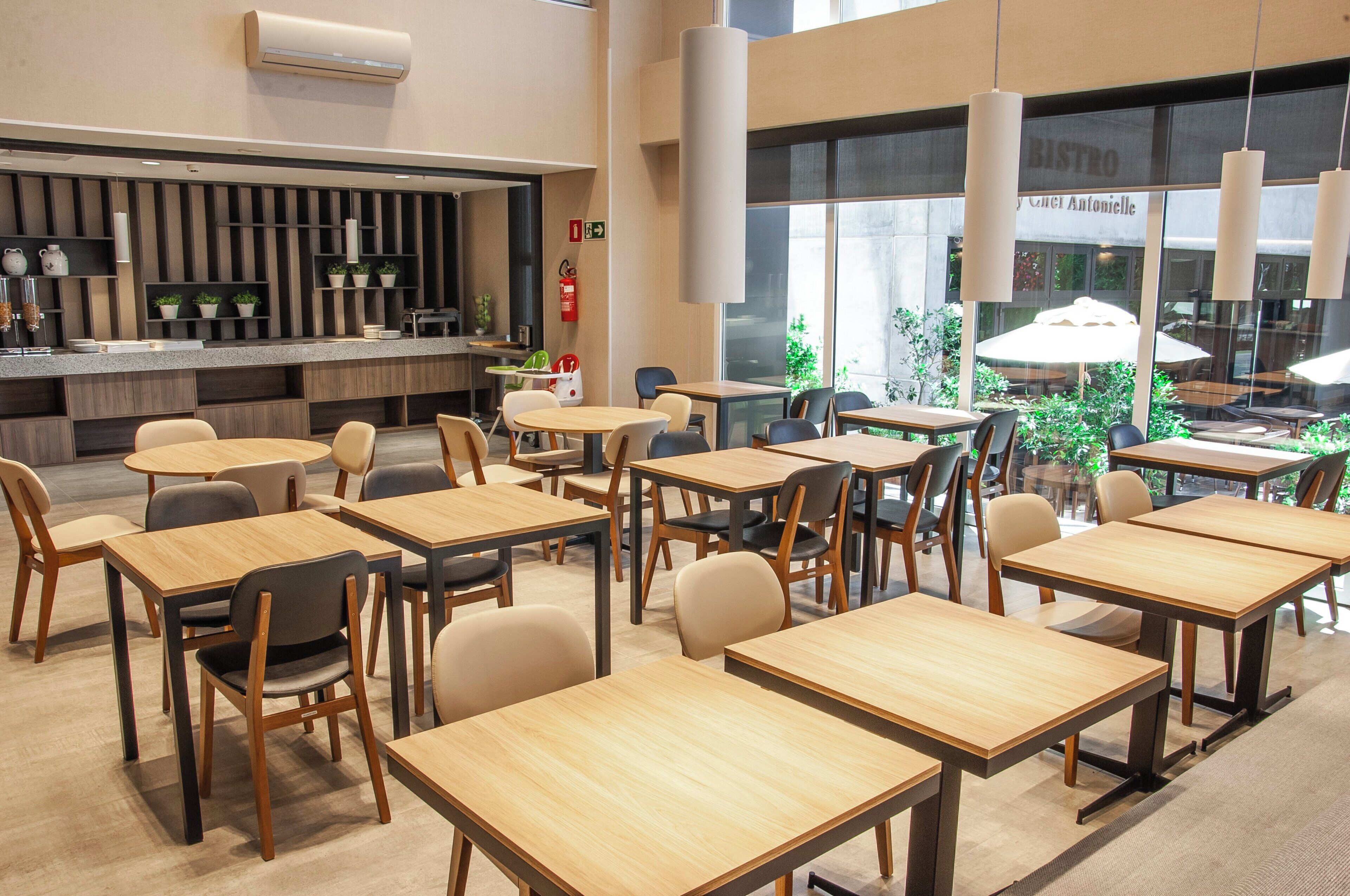 A modern cafe interior with multiple tables and chairs, a counter with a coffee machine, and large windows offering a view of the outdoors.