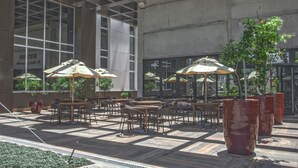 An outdoor seating area with tables and chairs, umbrellas, and potted plants.