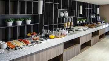 Una mesa de buffet con diversos alimentos y bebidas, que incluye frutas, cereales y refrescos.