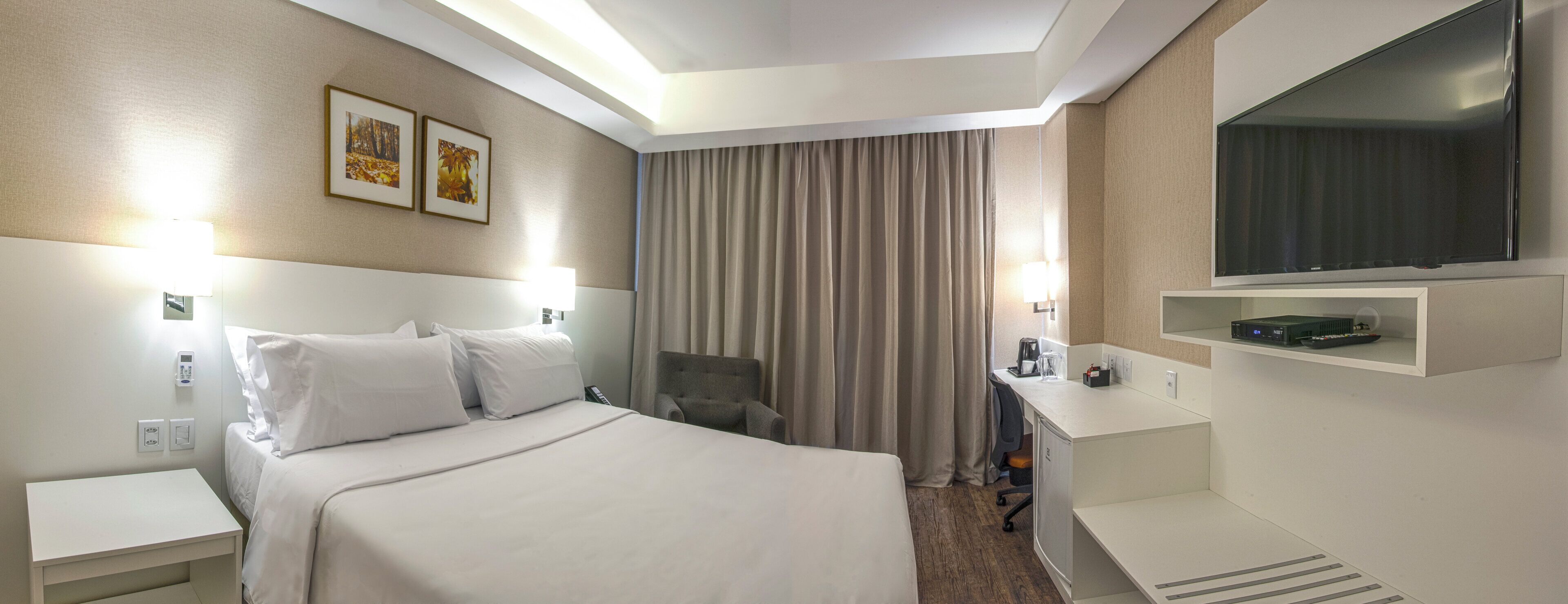 A hotel room with a bed, a desk, a television, and a window with curtains.