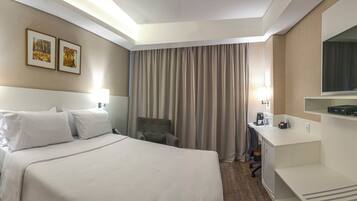 A hotel room with a bed, a desk, a television, and a window with curtains.