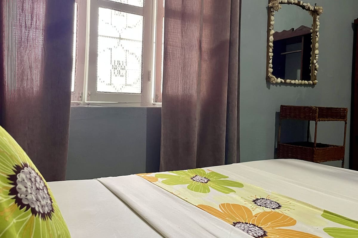 A bedroom with a bed, a window with curtains, a mirror, and a chair.