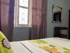 A bedroom with a bed, a window with curtains, a mirror, and a chair.