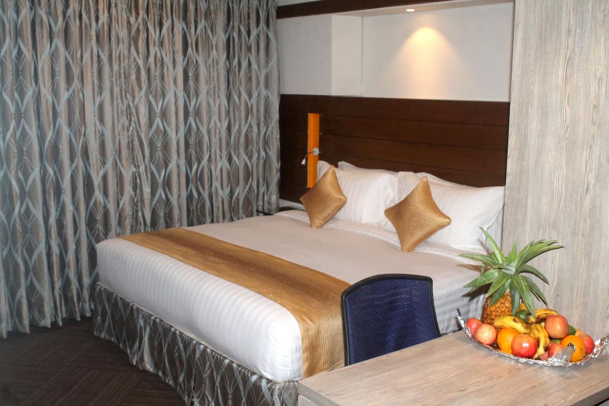A hotel room with a neatly made bed, a wooden headboard, and a fruit bowl on the side table.