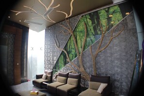 A modern lounge area with a large mural of a forest, a sofa with cushions, and a coffee table.