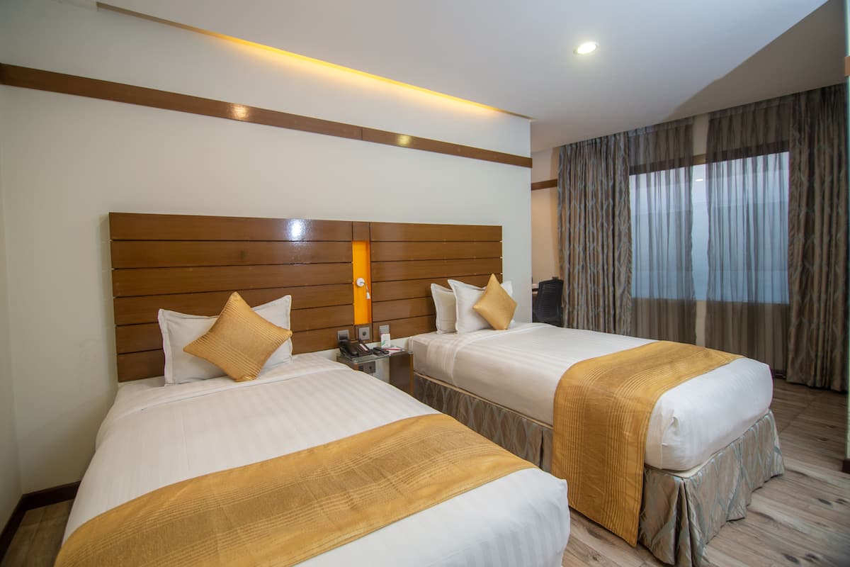 A hotel room with two beds, a wooden headboard, a nightstand, a telephone, and a window with curtains.