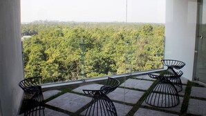 Un balcon donnant sur une forêt dense, avec une porte vitrée et deux chaises noires.