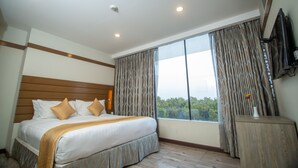 Une chambre d’hôtel avec un grand lit, une tête de lit en bois, une fenêtre avec des rideaux, une table de chevet et un téléviseur à écran plat.