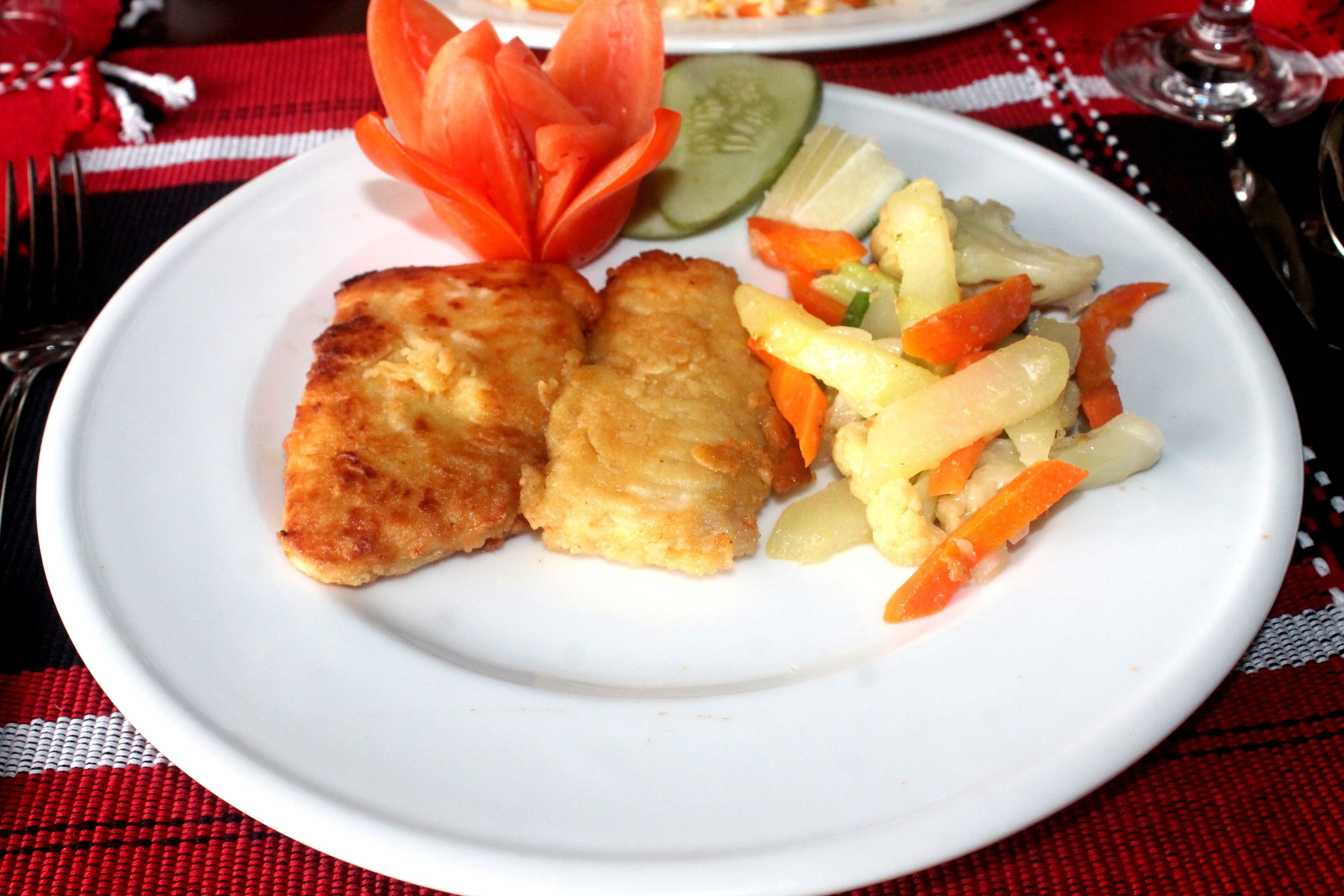 A plate with two pieces of breaded fish, a vegetable salad, and a decorative flower on a white plate.