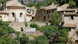 A historic village with stone buildings, a church with a cross, and a stone bridge. - Camping Le Botanic (Fabregues)