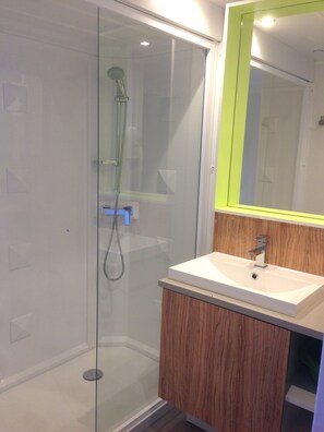 Une salle de bain moderne avec une douche à parois de verre, un meuble-lavabo en bois et un miroir avec un cadre vert.