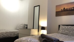 A hotel room with two beds, a dresser, a mirror, and a painting of a pier. - Ruskin Place (Crewe)