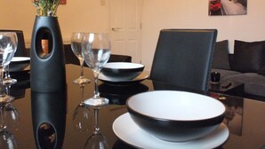 A dining table set with black bowls and wine glasses, a vase with flowers, and a painting of a red bus on the wall. - Ruskin Place (Crewe)