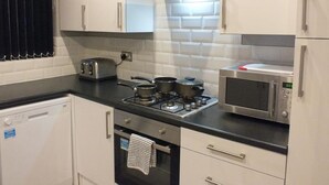 A modern kitchen with white cabinets, a gas stove, a microwave, and a toaster. - Ruskin Place (Crewe)