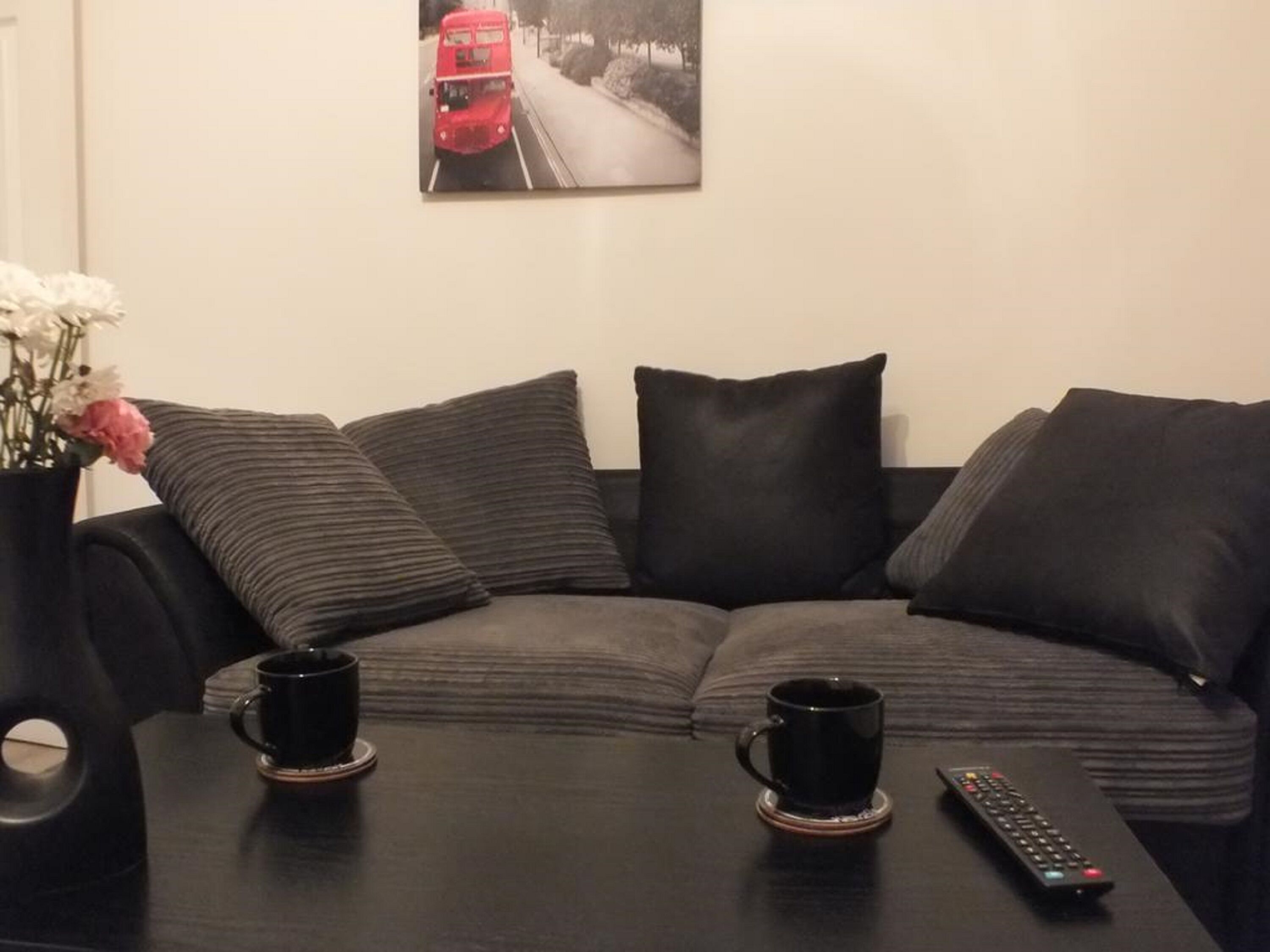 A modern living room with a sectional sofa, two black coffee mugs on a coaster, and a remote control on a table.