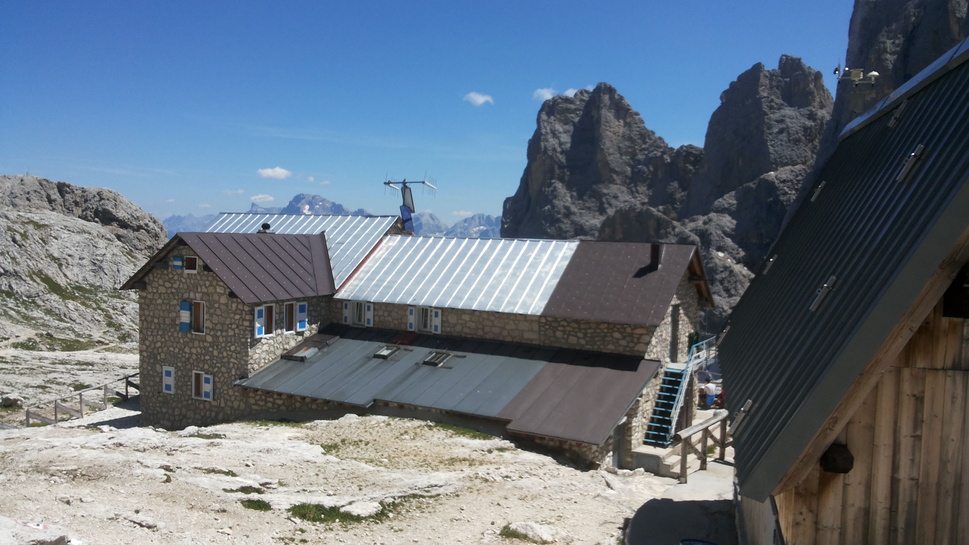 Un edificio de piedra con techo metálico, rodeado de terreno rocoso y montañas.