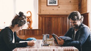 A cozy wooden interior with a dining table set for two, featuring a book, a mug, and a small dog figurine. - Rifugio Mulaz (Falcade)