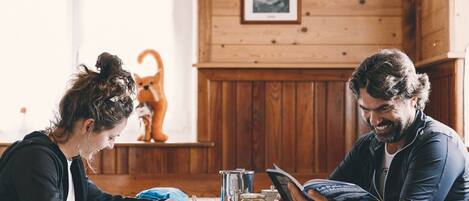 A cozy wooden interior with a dining table set for two, featuring a book, a mug, and a small dog figurine.